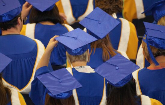 Graduates in blue caps and gowns celebrating at a graduation ceremony.