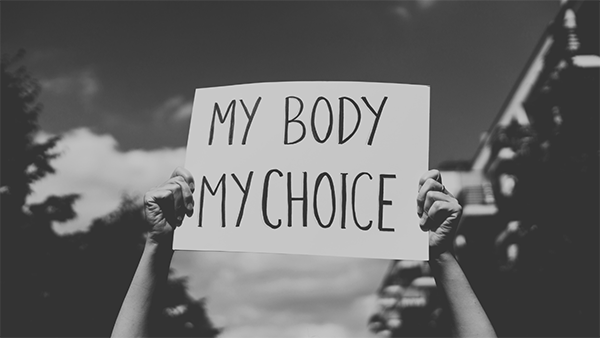 A person holding a sign that reads "MY BODY MY CHOICE" against a cloudy sky.