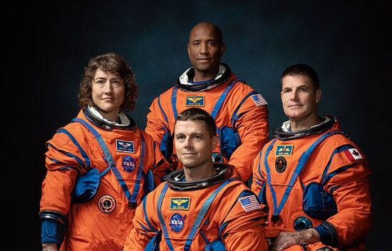 Four astronauts in orange space suits pose together against a dark background.