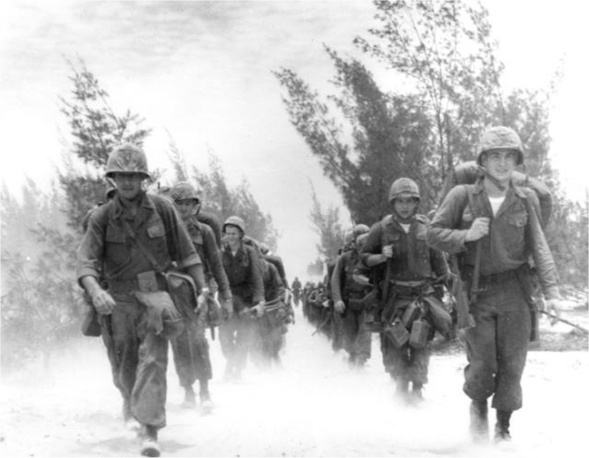 Two rows of U.S. Marines march down a road.