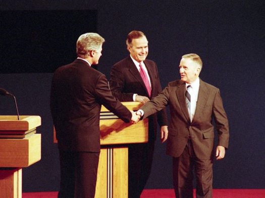 Ross Perot shakes hands with Bill Clinton. President Bush stands beside Perot.