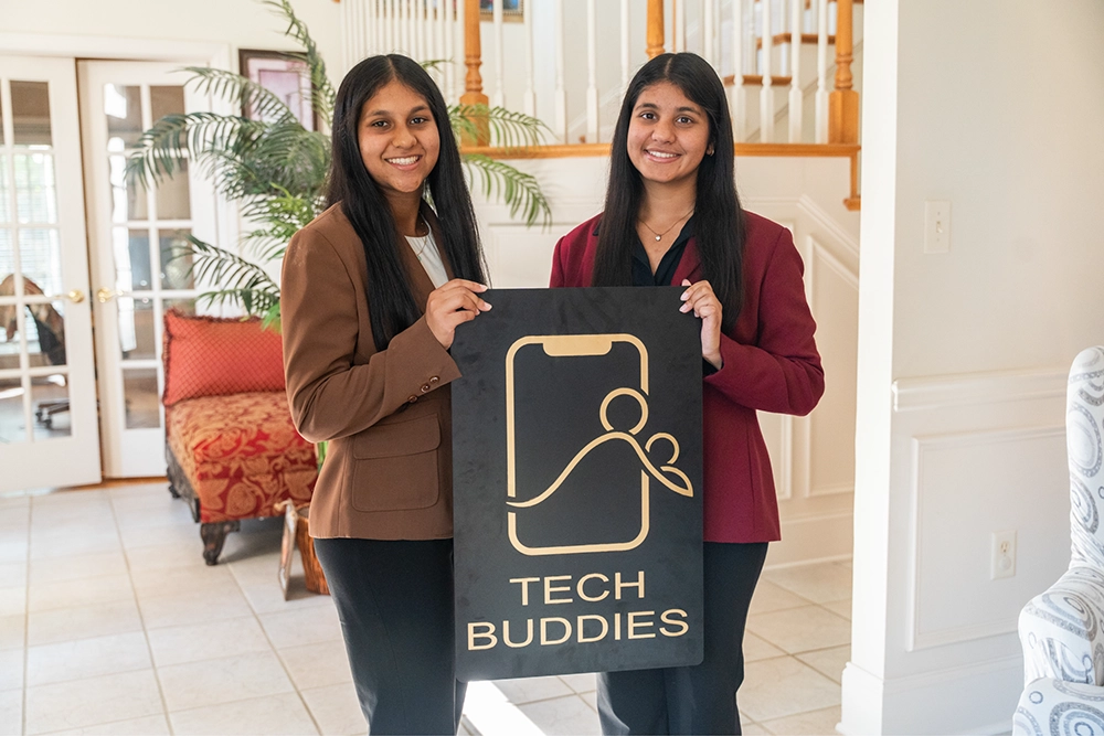 Medha and Reshma Lalani holding a Tech Buddies sign
