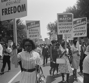 Black-and-white photo of a civil rights march with participants holding signs advocating for freedom and equal rights.