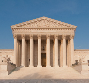 The façade of a large neoclassical building with columns and steps, under a clear blue sky.