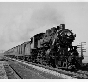 Black and white image of a steam locomotive pulling passenger cars along a railway track.