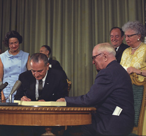 Lyndon B. Johnson signs legislation with several individuals present at a ceremonial event.