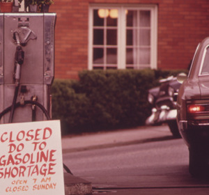 A closed gas station with a sign stating "Closed Due to Gasoline Shortage" in front of a parked car.