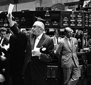 Black and white image of stock traders in a busy exchange, one man raising a paper while others observe.