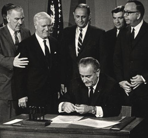 President Lyndon B. Johnson signing legislation, surrounded by six men, in a historic official setting.