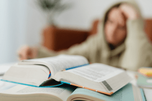A person appears stressed while studying with open textbooks on a table. The background is blurred.