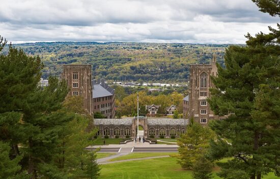 View of a college campus with historic buildings, trees, and hills under a cloudy sky.