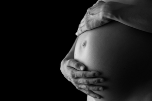 A close-up of a pregnant belly with hands gently cradling it, in black and white.