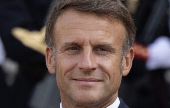 A man in a suit with short brown hair, smiling confidently at an outdoor event.