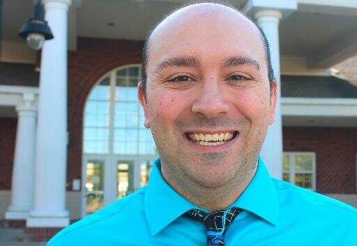 Smiling man in a blue shirt and tie poses in front of South Fayette High School.