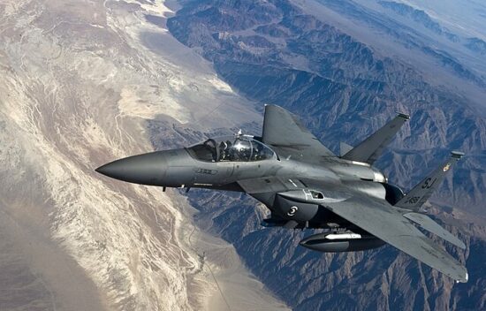 A military jet flying over a mountainous desert landscape.