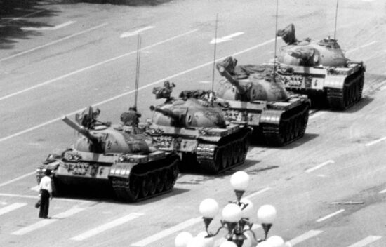 Military tanks on a street, with soldiers visible on top of the vehicles, during a historical military display.