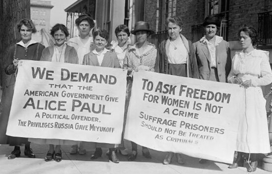 Women holding banners demanding freedom for suffragists and political rights, in early 20th-century setting.