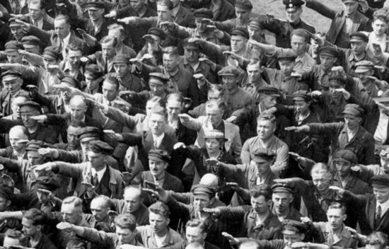 A large group of men performing a salute with their arms extended forward.