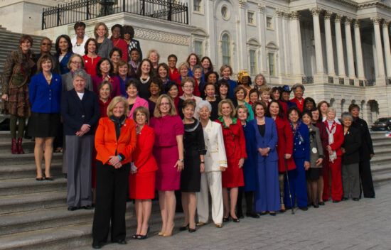 Group of women in colorful attire posing on the steps of a large building, likely a government or legislative structure.