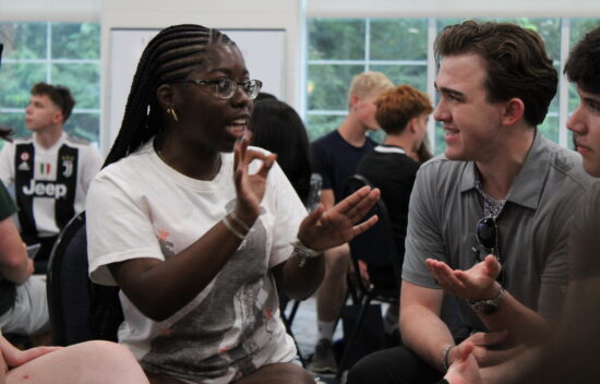 A diverse group of young adults engaged in a discussion, with one person gesturing while speaking.