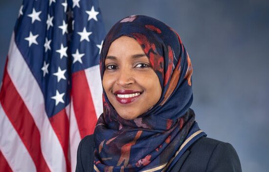 A woman in a headscarf smiles, posed in front of an American flag.