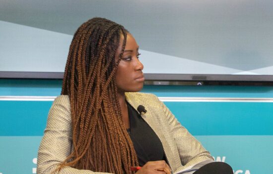 A woman with long braided hair listening attentively during a panel discussion.