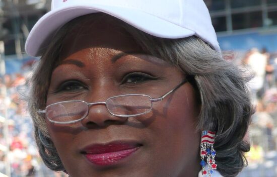 Woman wearing a white "Obama '08" cap and glasses, with earrings featuring red, white, and blue colors.