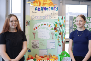 Two students standing beside a colorful project display about community versus abandonment.