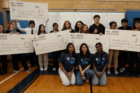 Students and representatives holding large checks for various awards and initiatives at a Bill of Rights Institute event.