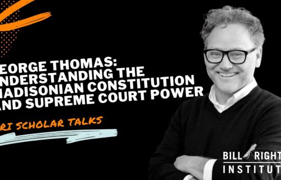 A man with glasses and curly hair smiles, discussing the Madisonian Constitution and Supreme Court power.