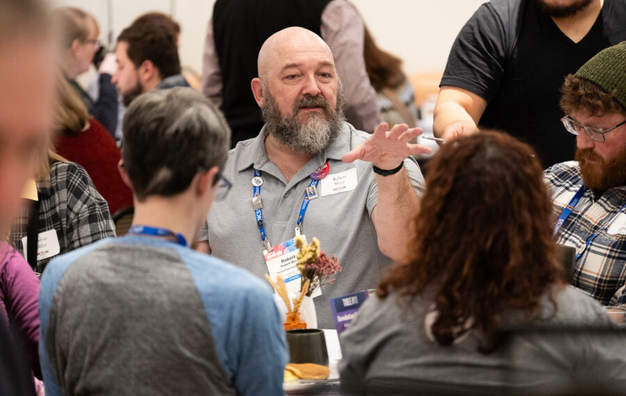 A group of people seated at a table, with one man gesturing while speaking during a discussion.