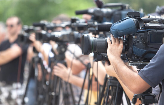 A row of cameras and operators at an outdoor event, focused on capturing video footage.