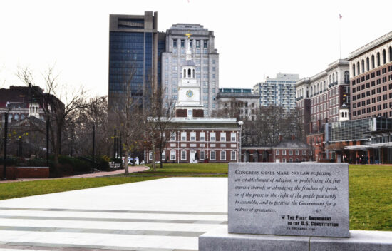 View of Independence Hall with a stone inscription of the First Amendment in the foreground, surrounded by city buildings.