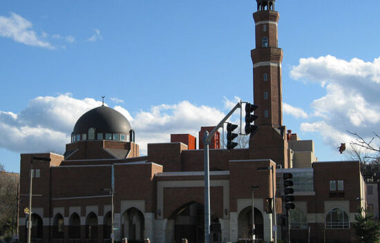 Brick mosque with a dome and minaret, set against a blue sky and scattered clouds.