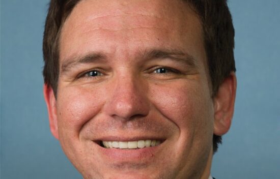 Portrait of a man in a suit, smiling, with short dark hair and blue eyes against a light blue background.