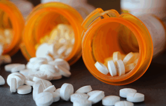 Close-up of spilled white pills from prescription bottles on a dark surface.