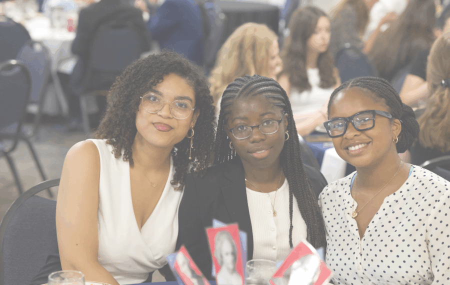 Three young women pose together at a dining table during an event, smiling for the camera.