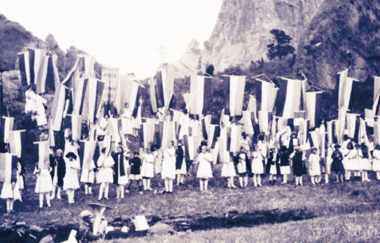 A historical black and white image of a large group of people in white attire holding long banners outdoors.