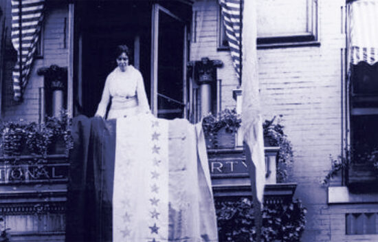 A woman stands on a balcony decorated with flags and a large fabric banner, in front of a building labeled "NATIONAL PARTY."