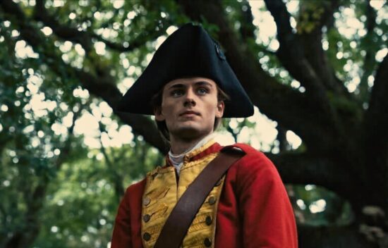 Man in a historical red military uniform riding a horse through a wooded area.