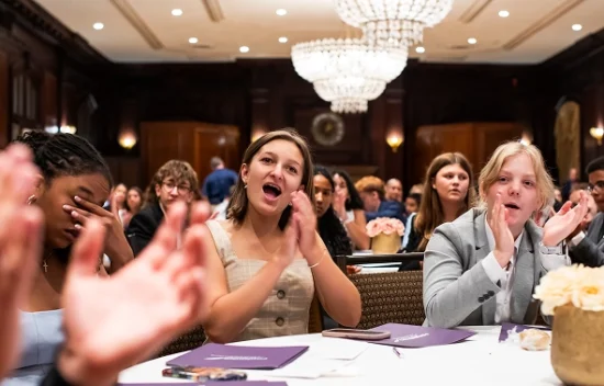 Group of people in a formal setting, some clapping and expressing enthusiasm during an event.