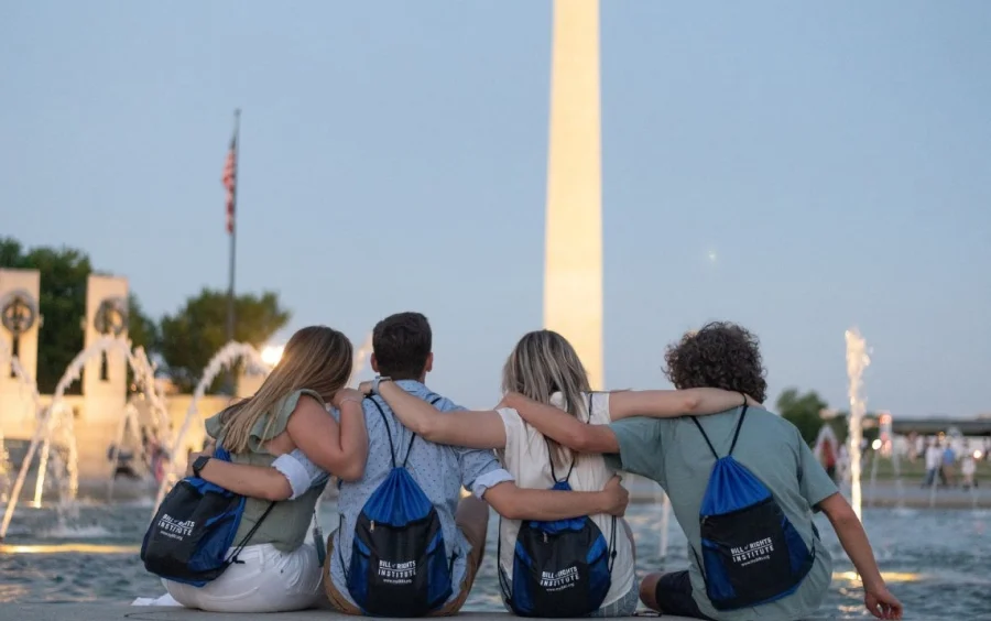 Four people sitting together by a fountain, gazing at the Washington Monument at dusk.
