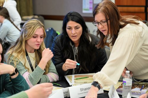 Three women engaged in a discussion at a table, examining documents and sharing insights.
