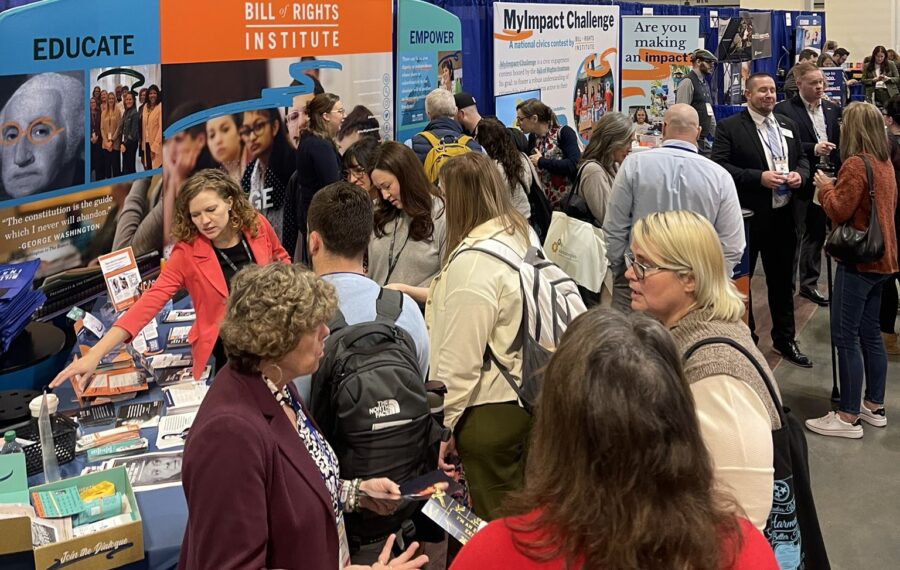 Crowd of people engaging at a booth in an exhibition hall with displays about education and advocacy.