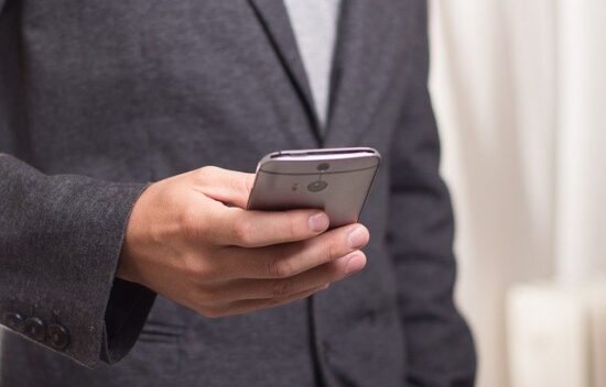 A person holding a smartphone in their right hand while wearing a dark blazer.
